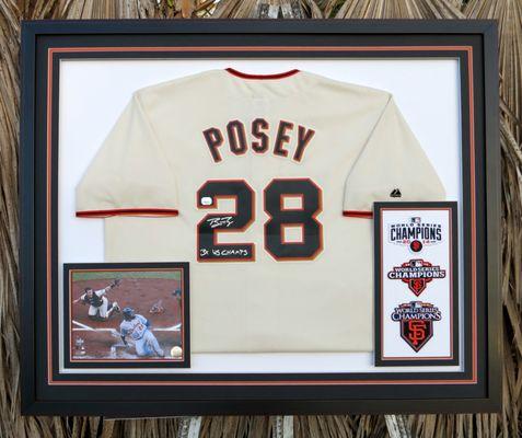 A signed photo and three patches, framed with mats which have beveled outside edges, mounted atop a jersey.