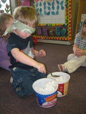 While learning about the five senses, this child is using a spoon to move cotton balls from one container to the next.