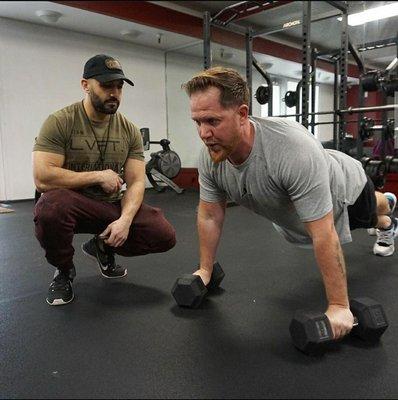 Personal trainer, Masi is supervising his client's form to make sure he's holding it during the entire set.