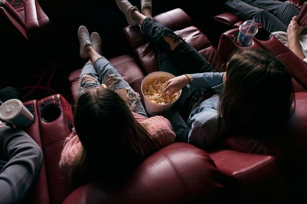 An adult woman sitting with her daughter in a movie theatre while eating popcorn.