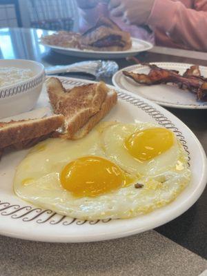 Sunny side up eggs, toast, and grits