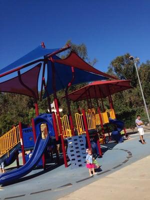 Playground has rubber surface for barefoot kids & soft landings. Small sand box on the RT corner of the structures + water fountain nearby.