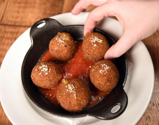 Pesto Arancini (rice balls) filled with fresh mozzarella, on a spicy marinara sauce