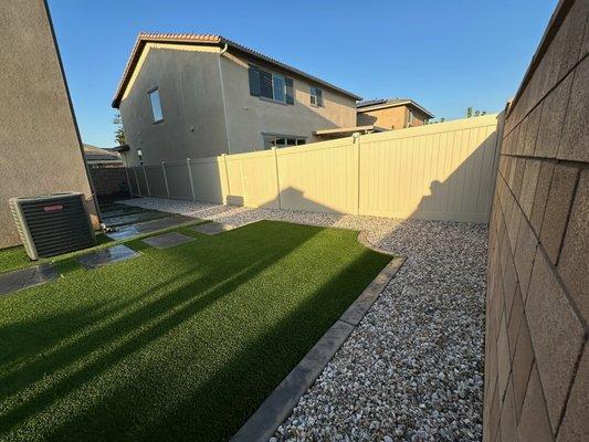 "Low-maintenance backyard with turf, stepping stones, and a gravel border for a clean, modern finish."