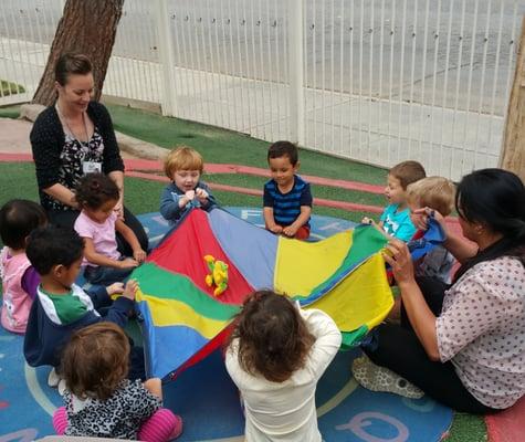 Parachute play helps with fine and gross motor skills, while encouraging children to track the colors the stuffed frog will land on.