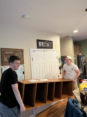 Owners Brett and Zack move a large bookcase carefully.