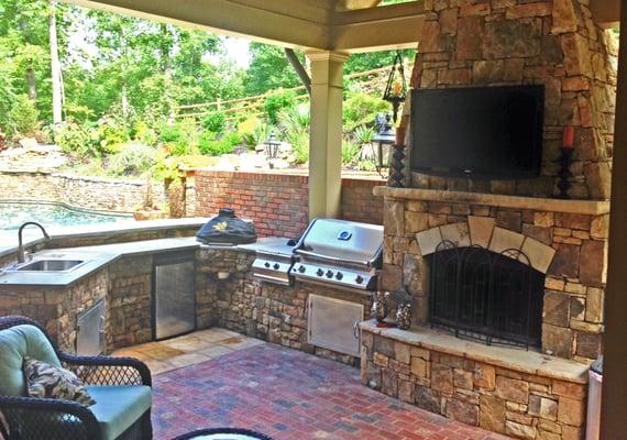 Outdoor Living at its Best. Roof Structure with Stone Fireplace and Kitchen overlooking several stone patios, pool and dining