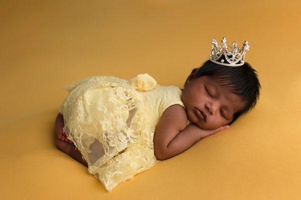 newborn photoshoot baby girl posed on yellow backdrop princess crown