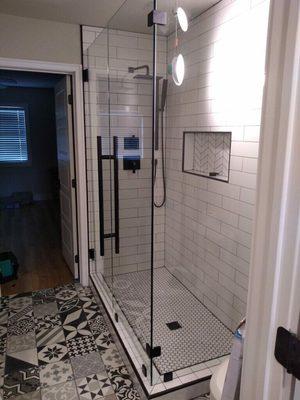 Frameless shower with matte black hardware and 36" ladder style handle.