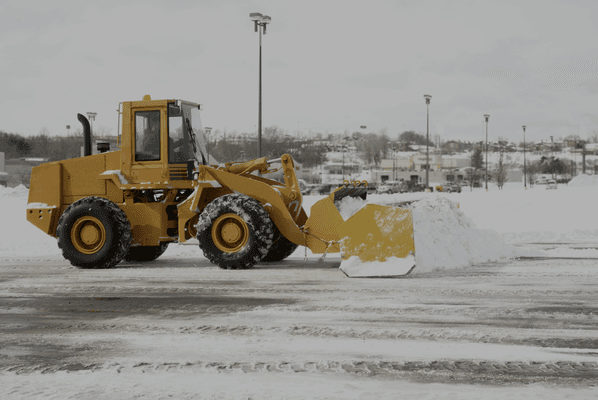 Small machine plowing snow in a parking lot.