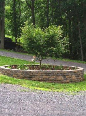 This is a circular retaining wall with perennial and annual plantings that transformed a dull grass island into a beautiful landscaped area.