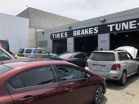 Cars parked for repairs out front, numerous and all in line for service.