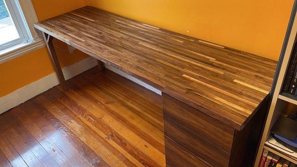 A wide desk featuring a walnut butcher block top and a 3 drawer cabinet.