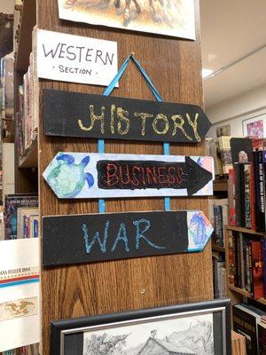 Signage directing shoppers to western, history, business, and war sections of bookstore