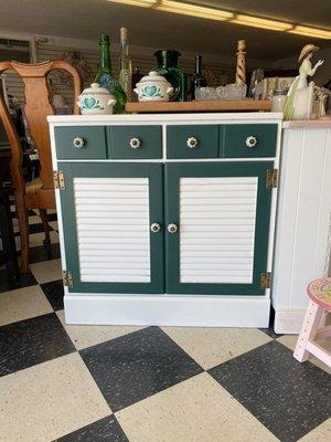 Small green and white storage cabinet with 1 shelf on the inside and two small drawers.