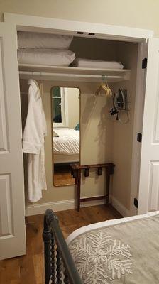 Closet with iron, luggage holder, mirror, and bath robe.