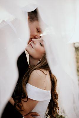 Bride and groom pose under veil after their wedding ceremony at The Kelley Farm Wedding venue in Bonney Lake, WA.