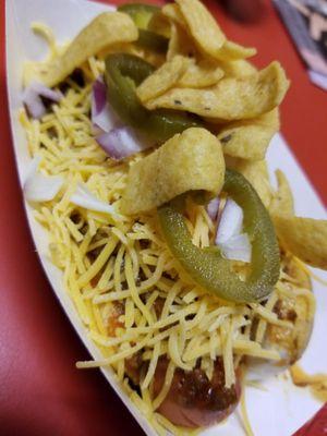 Chili dog topped with shredded cheese, onions, jalapenos and fritos