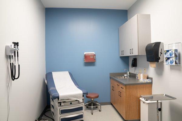 An exam room with an exam table, medical instruments hanging on the wall, a sink, and cupboards