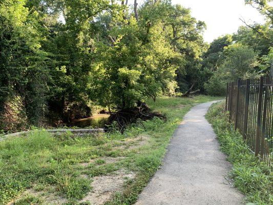 Asphalt path, creek on the left, houses on the right, some more manicured than others.