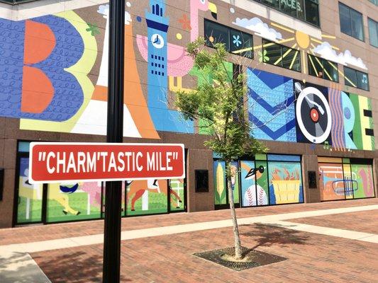 The 'Our Baltimore' Mural in front of the Iconic "Charm'tastic Mile" Street Sign.