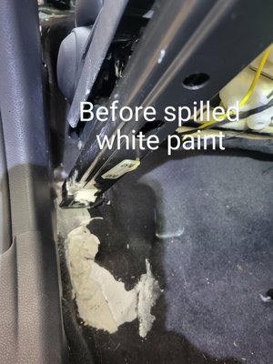 White paint was spilled under the passenger seat on black carpet