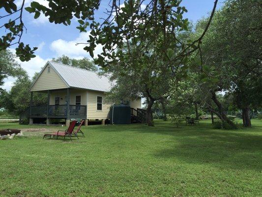 Our third guest rental home, the Green Jay Cottage, and its side yard with fire pit, outdoor grill, hammock, swings, and dining table