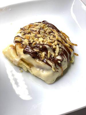 Turtle Cinnamon Roll topped with chocolate, caramel, and nuts