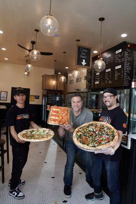 One of the partners and staff holding some of our selection of pizza