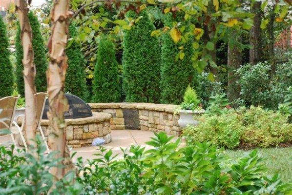 Firepit and bench on curved patio nestled in beautiful garden setting.