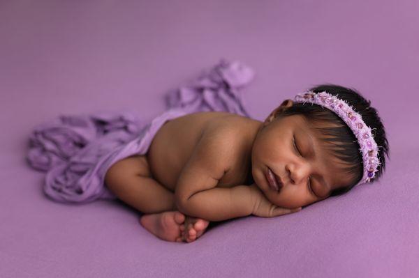 newborn baby girl sleeping on purple backdrop