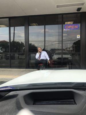 Sitting Outside smoking a cigar and talking on his cell phone. While 2 more men inside doing nothing.