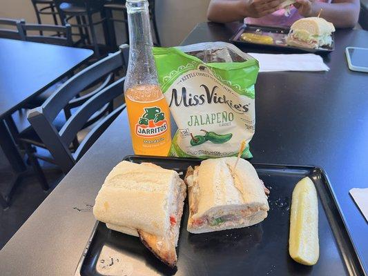 Spicy chicken jerk sandwich on a sourdough roll with jalapeno chips and cold Jarritos drink