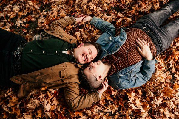 Rory and April lie on a field of autumn leaves, embracing.