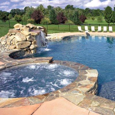 Free-form concrete pool with raised spa, flagstone coping, and rock grotto waterfall