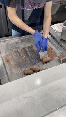 Ice cream being rolled. They pour cream onto the cold steel, then mix in toppings until it is perfectly frozen and ready to roll.