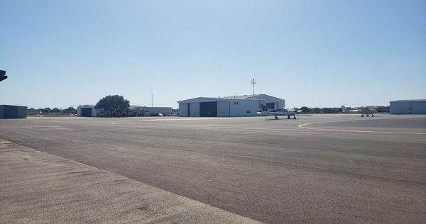 Coming off of taxiway, large white building is a maintenance facility,  brick building under trees is the FBO.