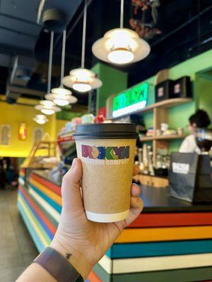 Hot coffee cup held in hand with the front counter in background.