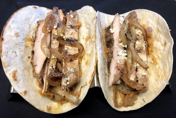 Fajita Chicken Tacos - Grilled marinated chicken on a flour tortilla with refried beans, rice, grilled onions, montequilla sauce, & cotija.