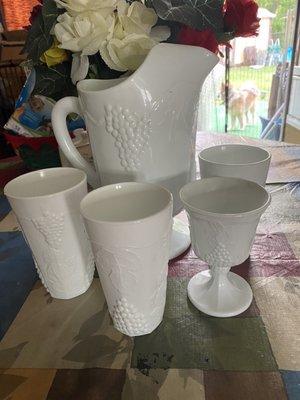 White porcelain pitcher and glasses and desert fishes with grapes on them along with gravy / soup dish