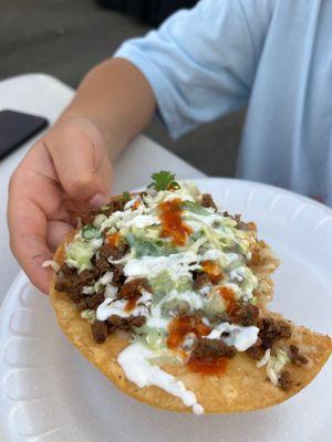 Taco vampiros (description: tostada with melted mozzarella, asada, cabbage, cilantro, crema, guacamole salsa, red and green salsa)