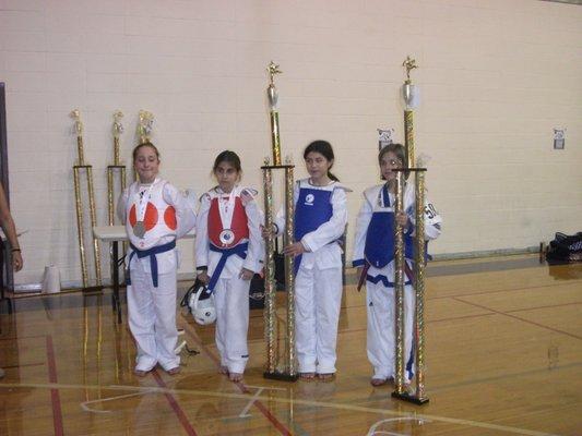 Miss CiCi (far right) as a blue belt with one of her many 6-7 foot trophies.