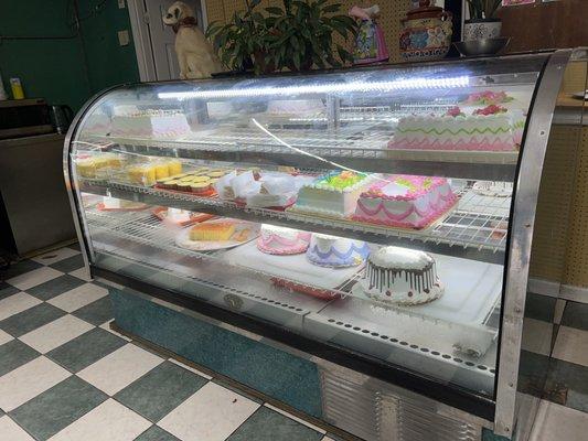 Cakes and desserts are in a refrigerated display case.