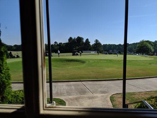 View of practice putting green and driving range from inside clubhouse.