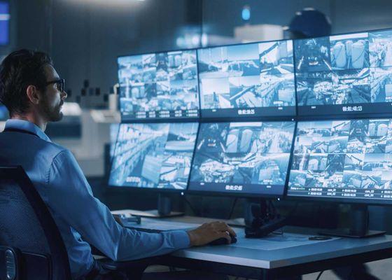 Security professional at a monitoring station sitting in front of a setup displaying multiple properties and cameras, for timely response.