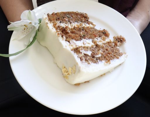 A slice of the 8" carrot cake with cream cheese frosting, real flowers, and light gold foil