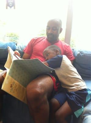 Daddy reading a book to his big boy on the super large comfy sectional in the children's area!