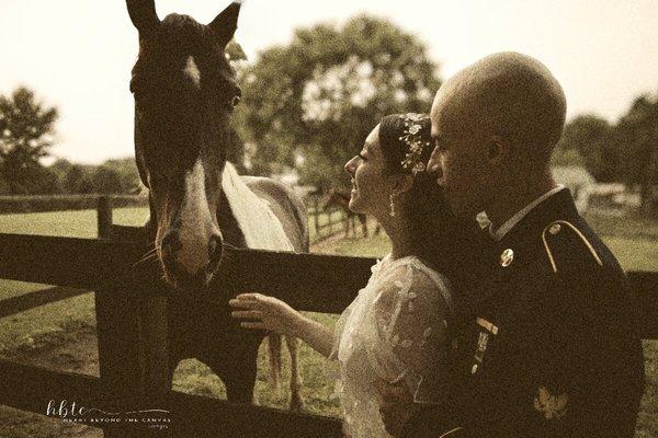 bride reaching to touch horse and groom in uniform holding her.