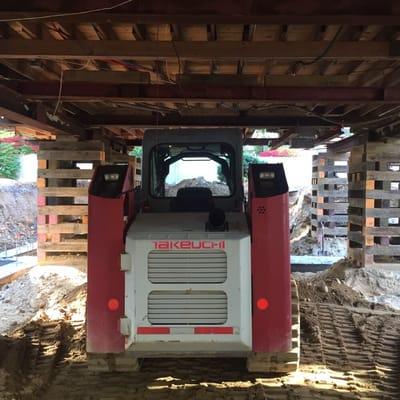 Digging under a raised house for a new foundation.