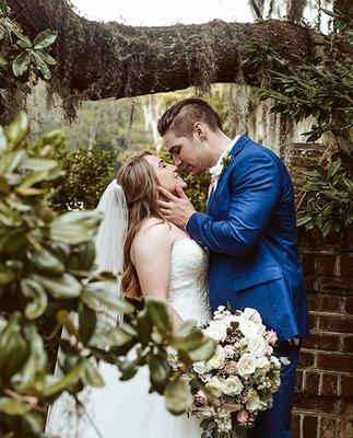 A newlywed couple kiss under a tree